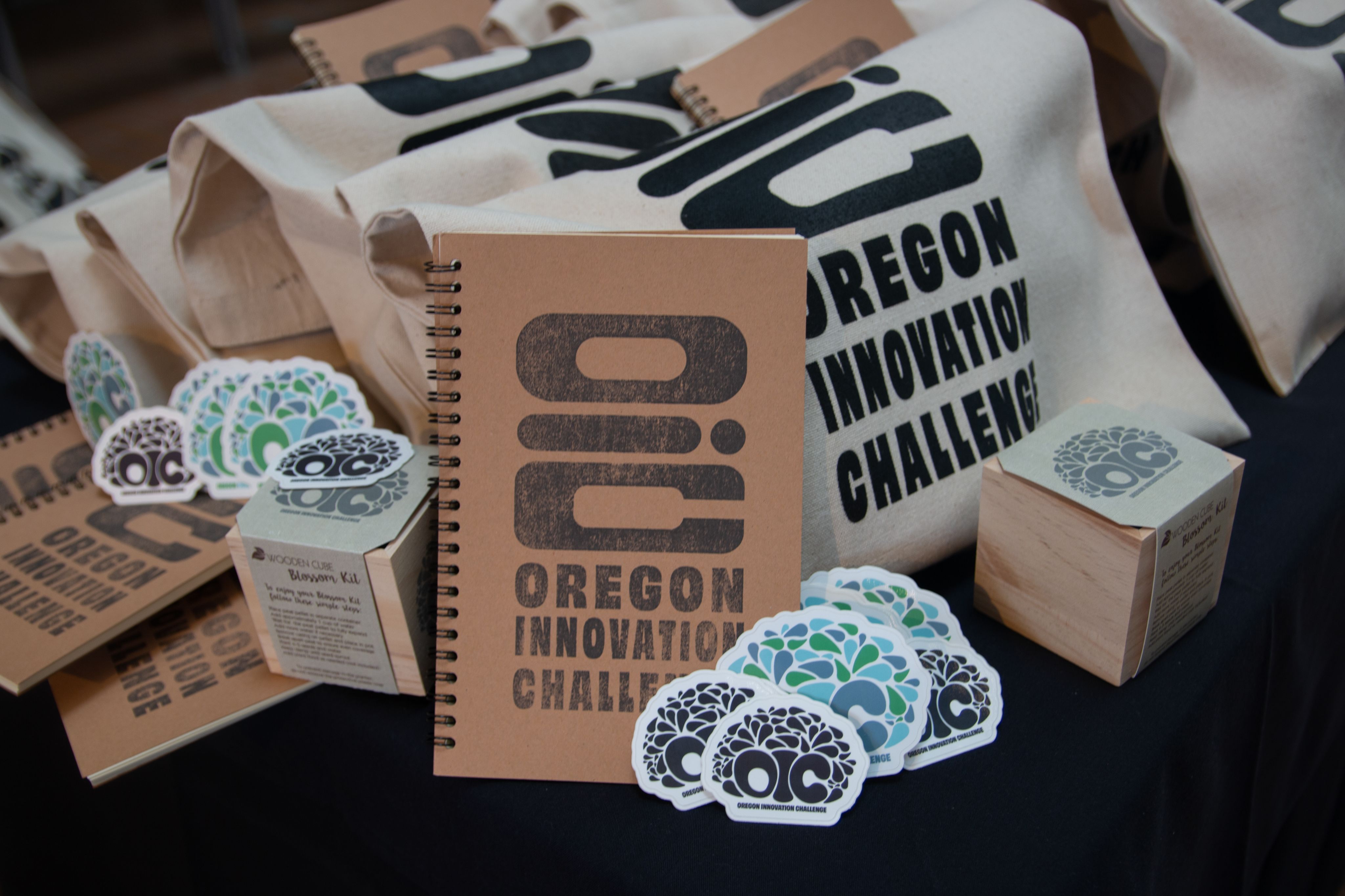 A photo of several Oregon Innovation Challenge promotional items including a notebook, stickers, and reusable bags.